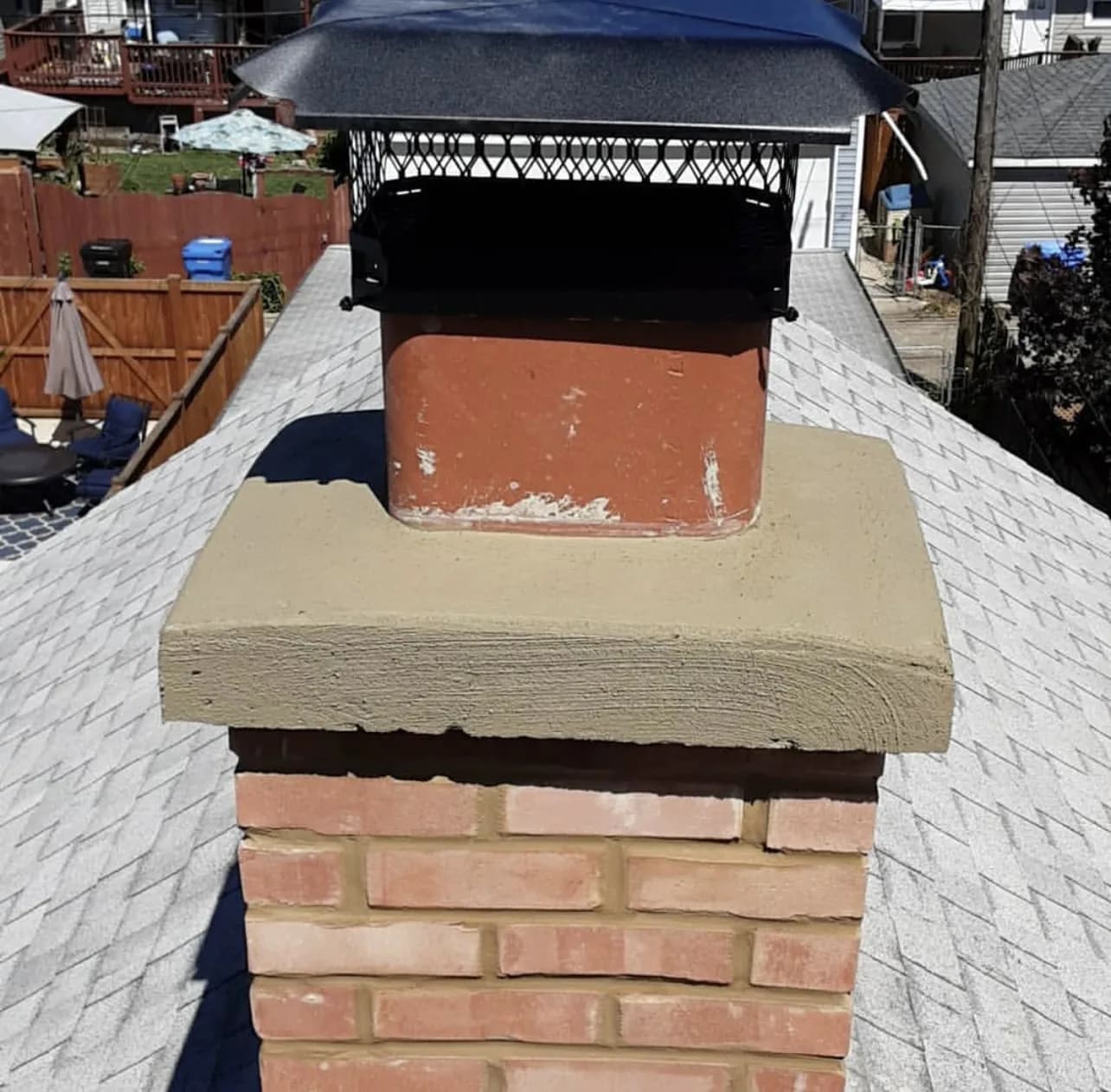 Freshly repaired brick chimney with new mortar crown and metal spark arrestor cap on a residential roof