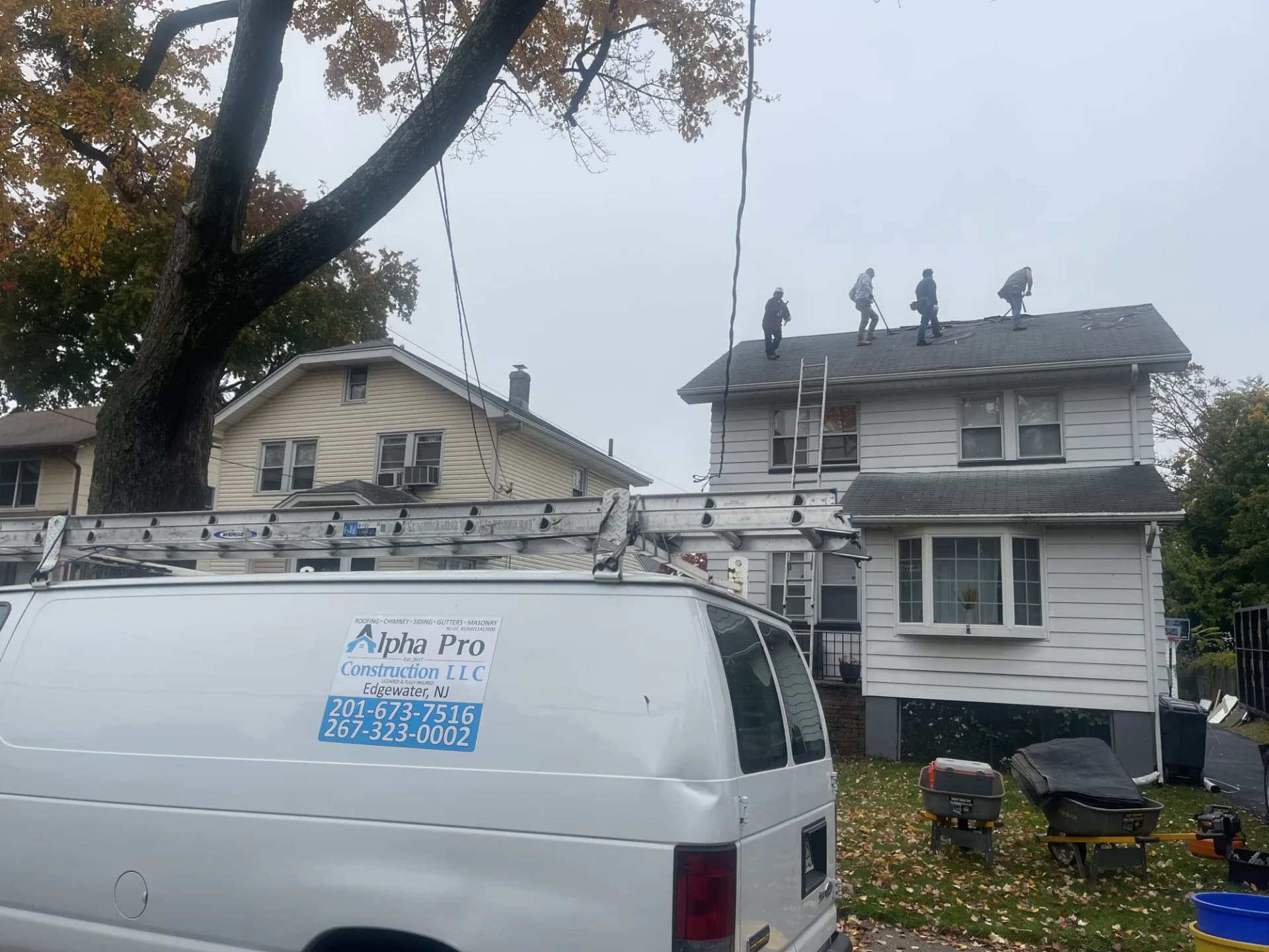Alpha Pro Construction crew and van beside a completed gray shingle roof in New Jersey