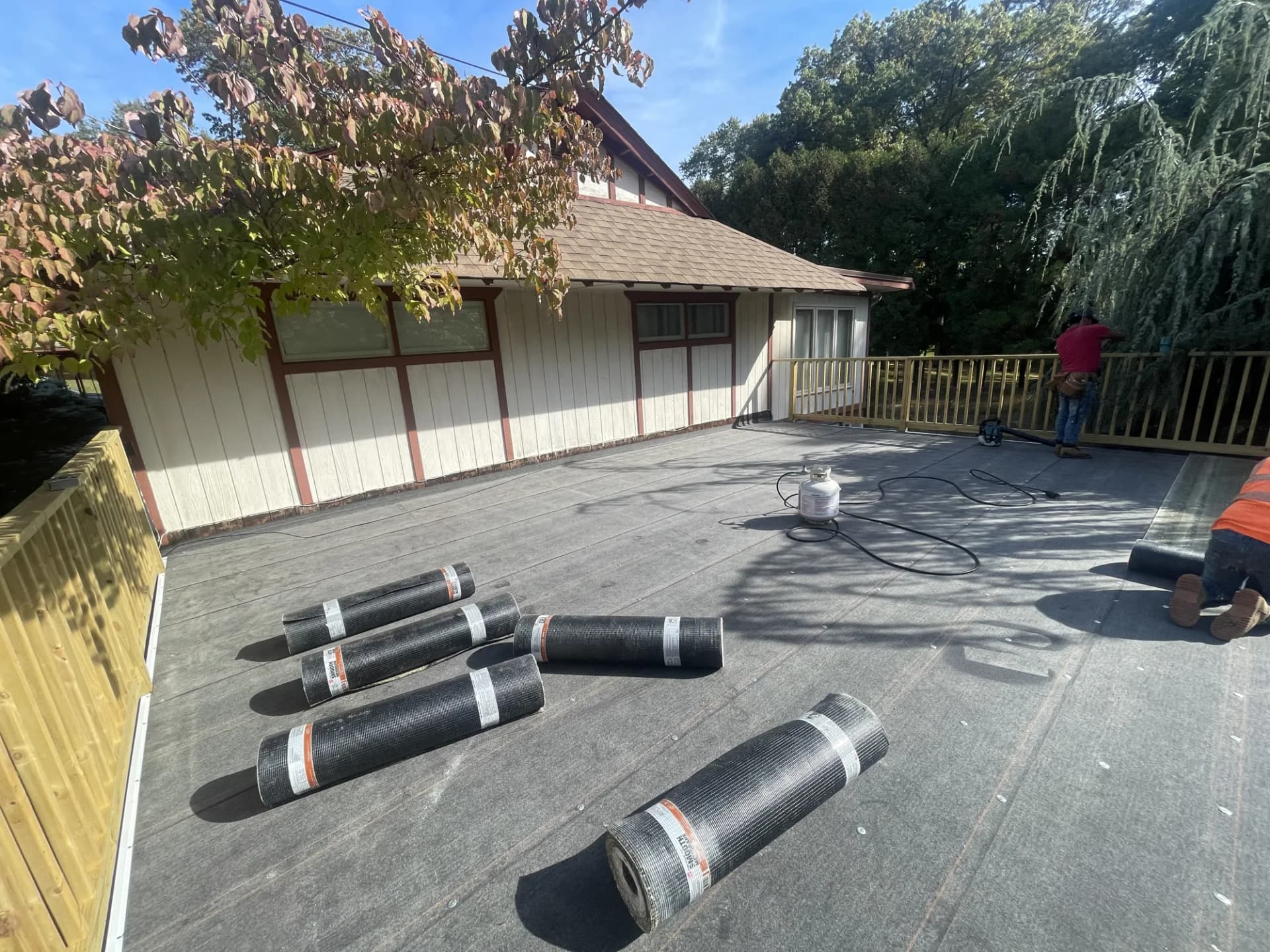 Rolls of torch-down modified bitumen roofing material staged on a flat roof deck in New Jersey before installation