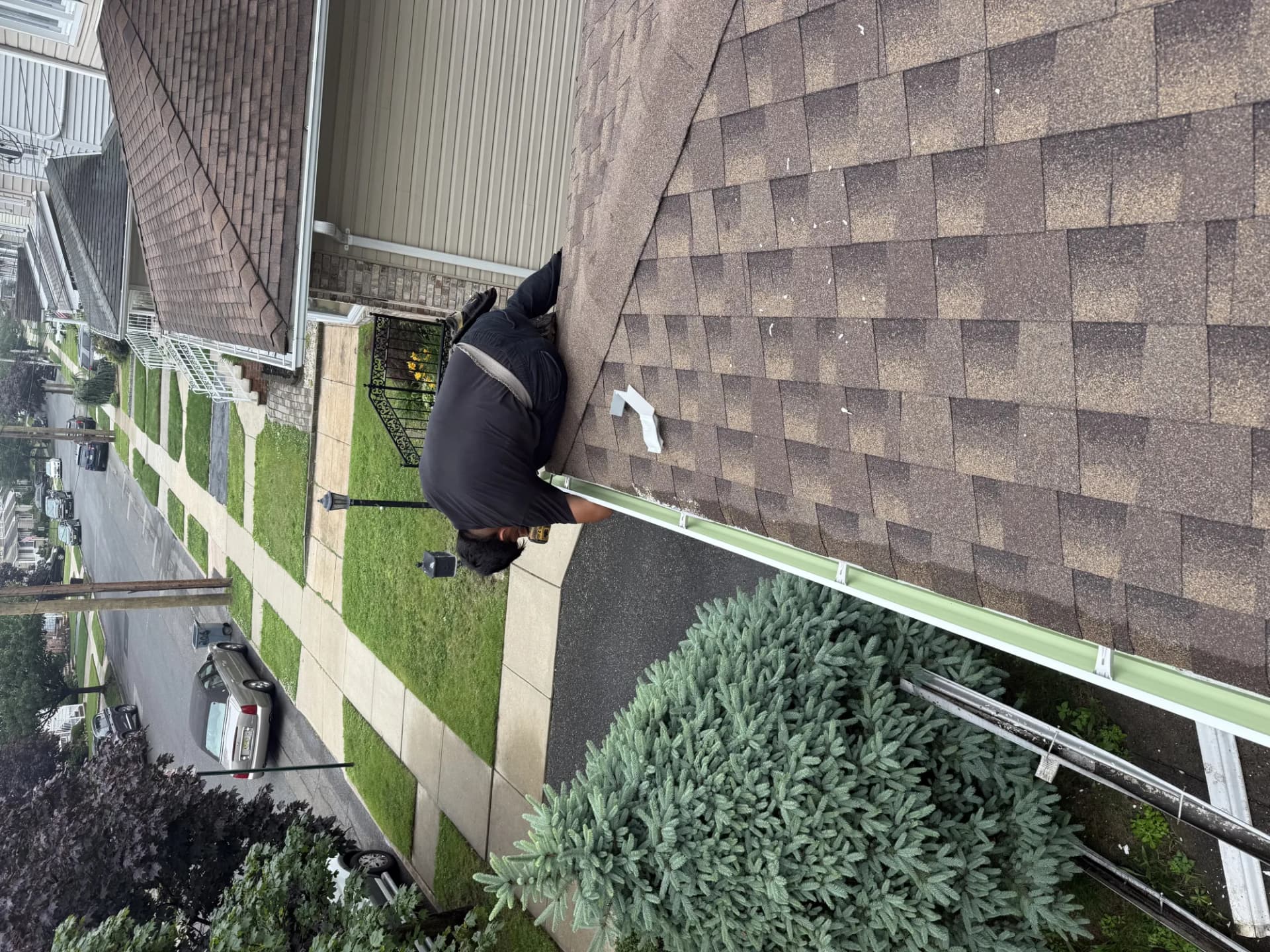 Technician on a ladder installing a white seamless aluminum gutter along the eave of a shingle-roofed home in New Jersey